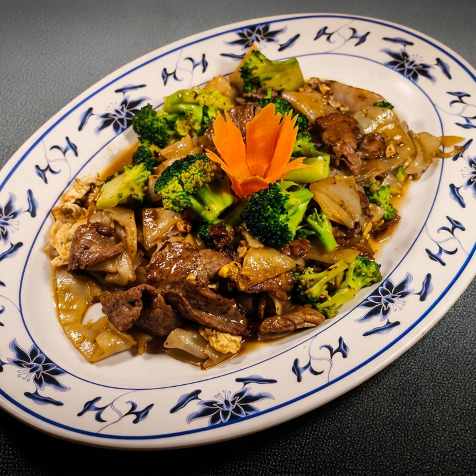 Stir-fried beef, broccoli, onions, and noodles garnished with a carved carrot flower on a blue-and-white oval plate.